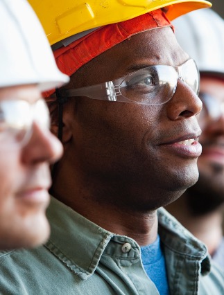 A man with safety goggles and hard hat looks up to the right